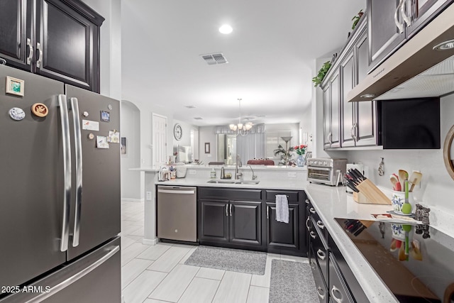 kitchen featuring visible vents, under cabinet range hood, a peninsula, stainless steel appliances, and a sink