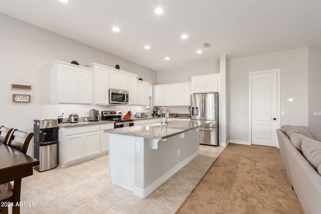 kitchen with white cabinets, an island with sink, light carpet, light stone countertops, and appliances with stainless steel finishes