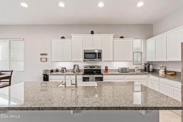 kitchen featuring appliances with stainless steel finishes, light tile patterned floors, a kitchen island with sink, stone countertops, and white cabinetry