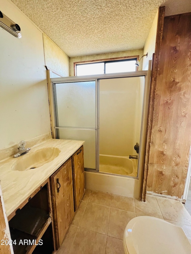 full bathroom featuring combined bath / shower with glass door, a textured ceiling, vanity, tile patterned flooring, and toilet