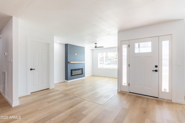 foyer with a ceiling fan, a large fireplace, light wood-style flooring, and baseboards