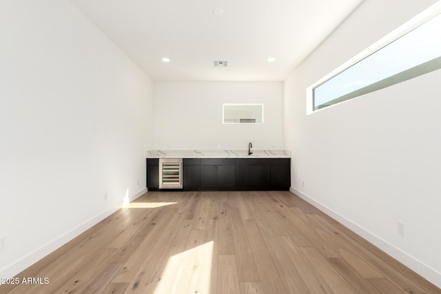 bar featuring a sink, light wood-type flooring, baseboards, and beverage cooler