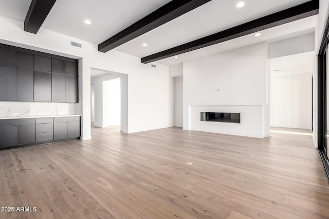 unfurnished living room with visible vents, recessed lighting, a glass covered fireplace, beamed ceiling, and light wood-type flooring