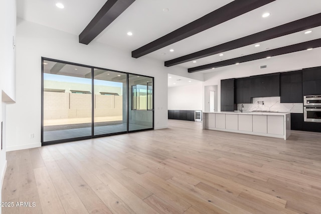 unfurnished living room with a sink, beam ceiling, light wood-style floors, and recessed lighting