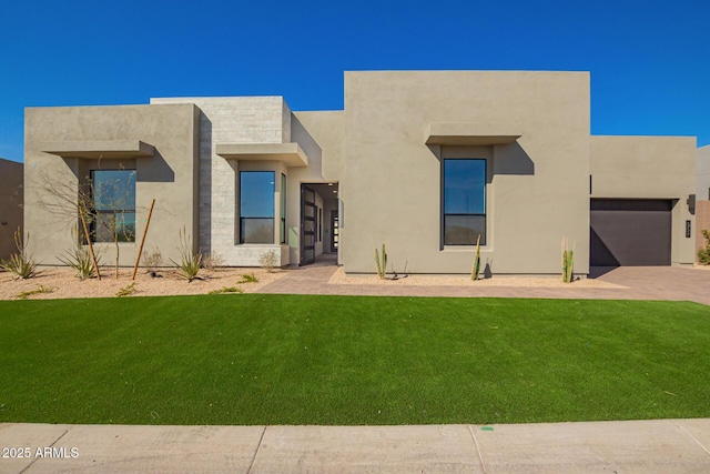 pueblo revival-style home featuring stucco siding, driveway, stone siding, a front yard, and a garage