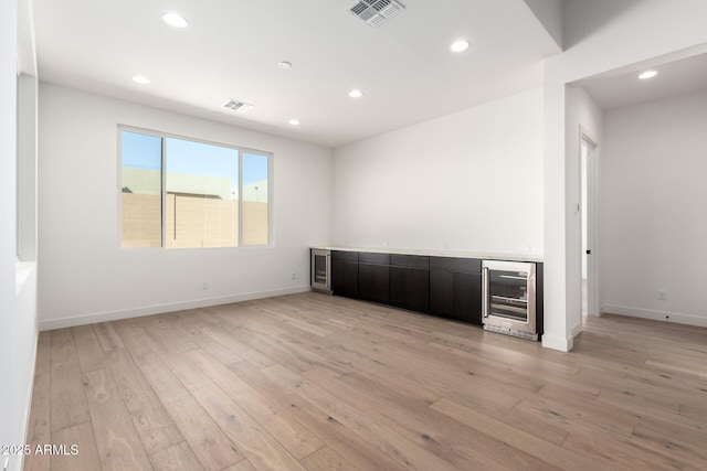 unfurnished room featuring wine cooler, visible vents, light wood-style flooring, and wet bar