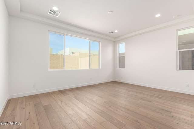 spare room featuring plenty of natural light, baseboards, visible vents, and light wood finished floors