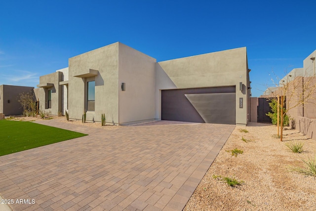 southwest-style home with stucco siding, decorative driveway, a garage, and fence