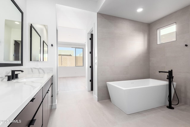 full bath with tile patterned flooring, a soaking tub, tile walls, and vanity