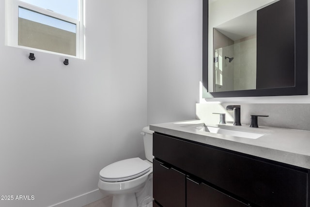 bathroom with vanity, toilet, baseboards, and a tile shower