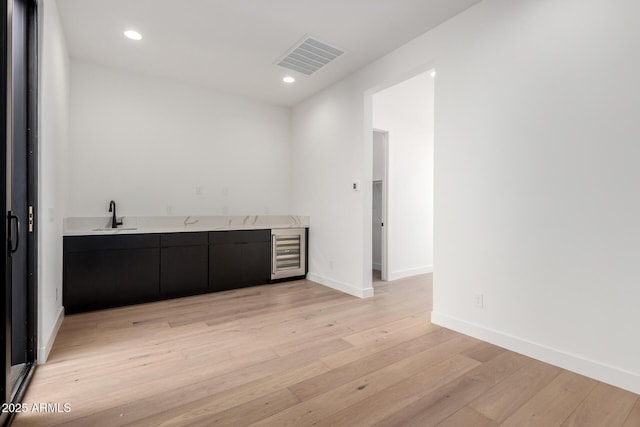 interior space with light wood finished floors, visible vents, wine cooler, wet bar, and a sink