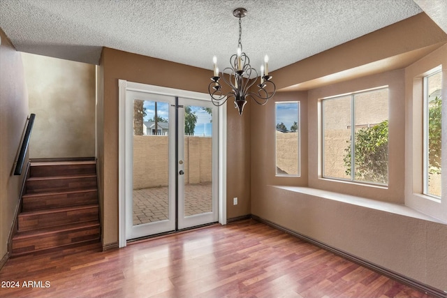 unfurnished dining area featuring hardwood / wood-style floors, an inviting chandelier, and a textured ceiling