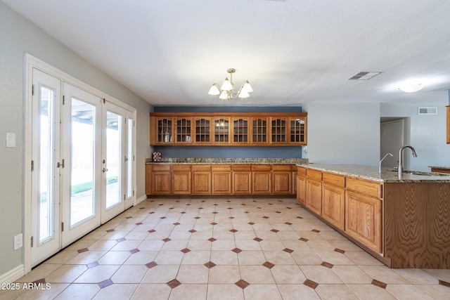 2338 E Javelina Ave, Mesa, AZ 85204 - kitchen with a peninsula, brown cabinets, a chandelier, light stone counters, and glass insert cabinets