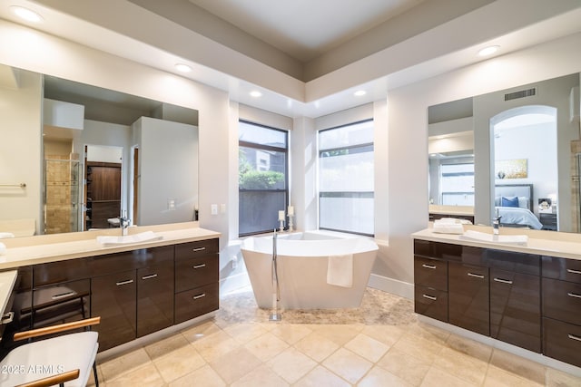 full bathroom with ensuite bath, a freestanding tub, two vanities, a stall shower, and a sink