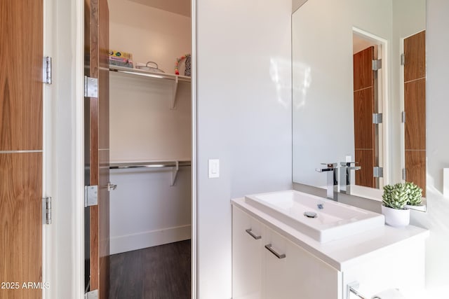 bathroom featuring a walk in closet, baseboards, wood finished floors, and vanity