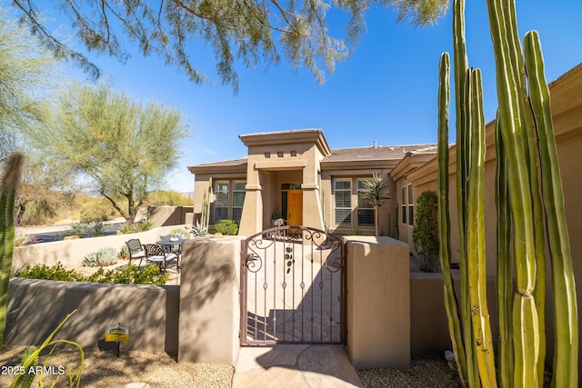 view of front of property with a fenced front yard, a patio, stucco siding, and a gate