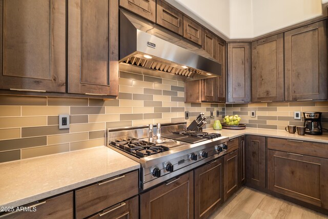 kitchen with light wood-type flooring, tasteful backsplash, dark brown cabinetry, stainless steel gas stovetop, and exhaust hood