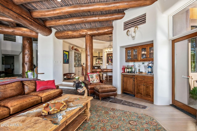 living room featuring beamed ceiling, light hardwood / wood-style flooring, bar area, and an inviting chandelier