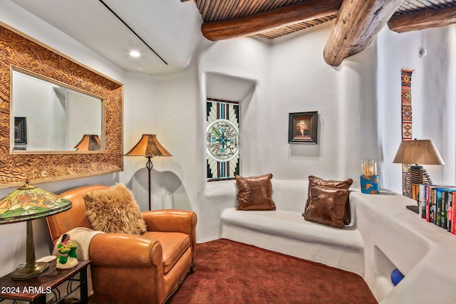 living area featuring beamed ceiling and dark carpet