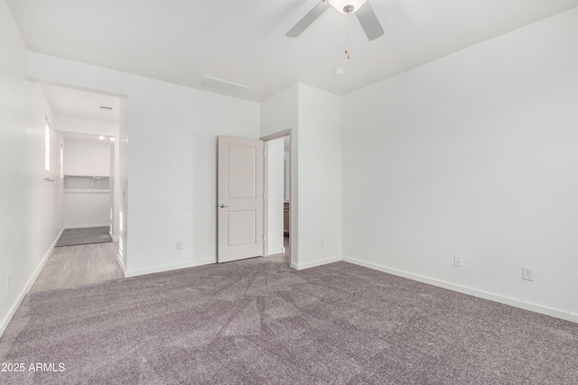 unfurnished bedroom with carpet floors, visible vents, a spacious closet, a ceiling fan, and baseboards