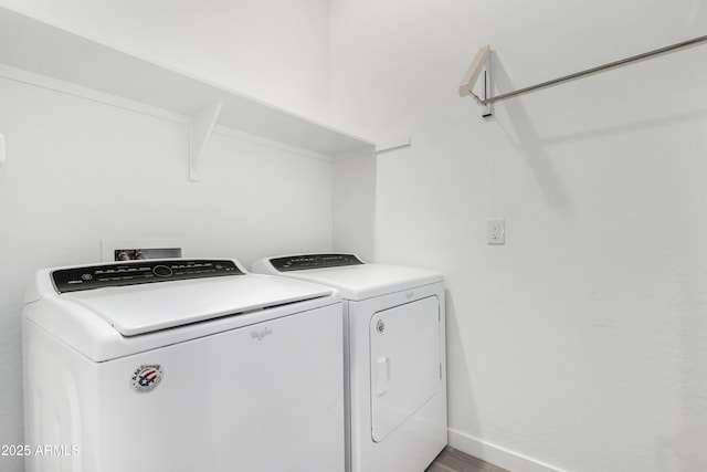 clothes washing area with laundry area, baseboards, wood finished floors, and washing machine and clothes dryer