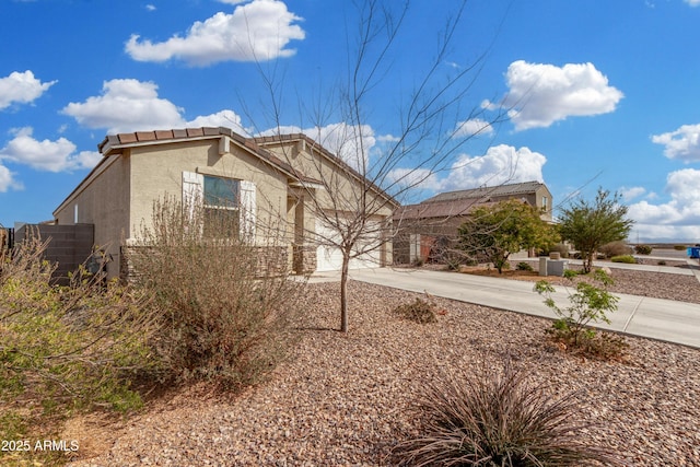 view of side of property featuring a garage, concrete driveway, fence, and stucco siding