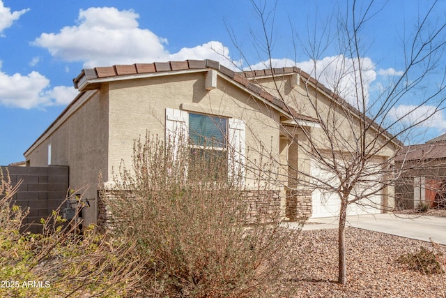 view of side of property featuring a garage, concrete driveway, a tiled roof, fence, and stucco siding