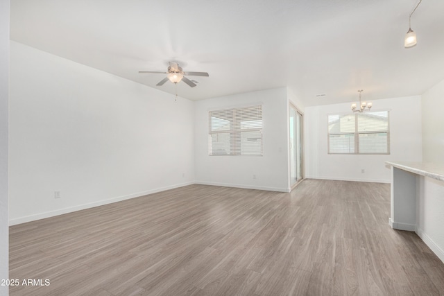 spare room featuring light wood-style flooring, baseboards, and ceiling fan with notable chandelier