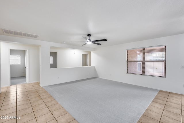 empty room featuring light tile patterned floors, visible vents, light colored carpet, and ceiling fan