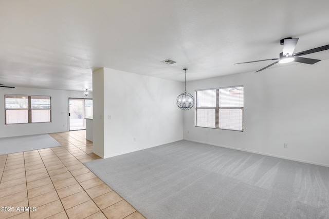 spare room with visible vents, light carpet, ceiling fan with notable chandelier, light tile patterned flooring, and baseboards