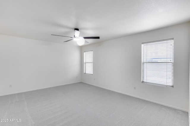 spare room with a ceiling fan, light colored carpet, and baseboards