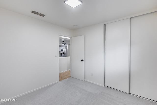 unfurnished bedroom with visible vents, baseboards, carpet, stainless steel fridge with ice dispenser, and a closet