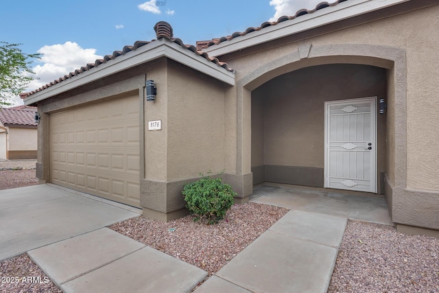 doorway to property with stucco siding, a garage, driveway, and a tiled roof