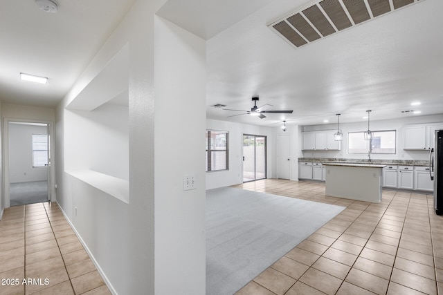 kitchen featuring visible vents, a center island, white cabinetry, light tile patterned floors, and a healthy amount of sunlight