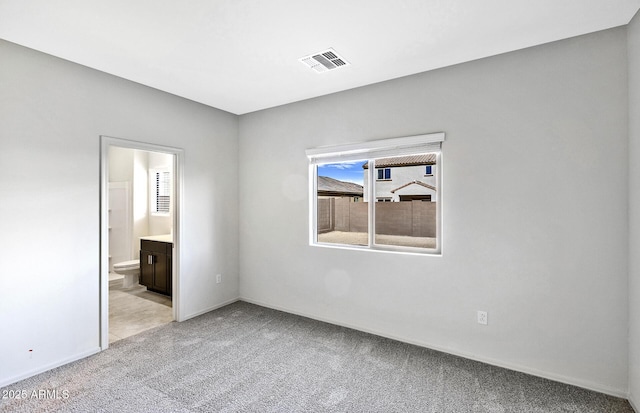 unfurnished bedroom with ensuite bath, light carpet, baseboards, and visible vents