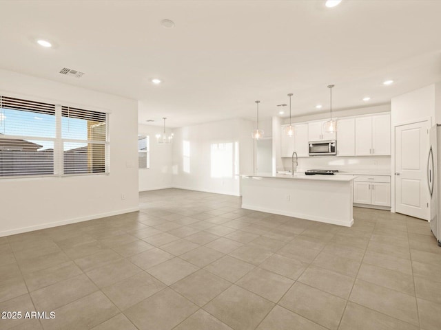 kitchen featuring a kitchen island with sink, an inviting chandelier, white refrigerator, decorative light fixtures, and white cabinetry