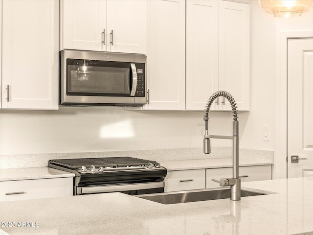 kitchen featuring white cabinets, stainless steel appliances, light stone countertops, and sink