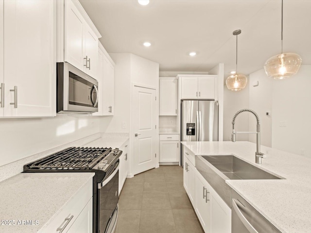 kitchen featuring light stone countertops, stainless steel appliances, sink, pendant lighting, and white cabinetry