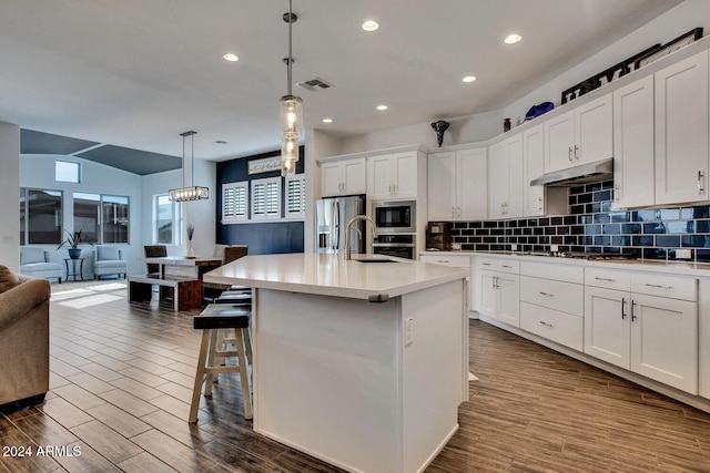 kitchen with appliances with stainless steel finishes, white cabinetry, hanging light fixtures, and an island with sink