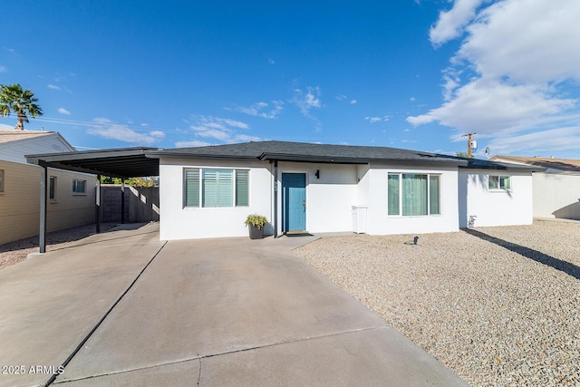 view of front of home featuring stucco siding, roof mounted solar panels, fence, a carport, and driveway