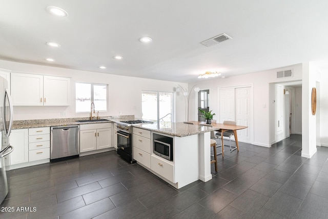 kitchen with a kitchen bar, appliances with stainless steel finishes, light stone counters, sink, and white cabinetry