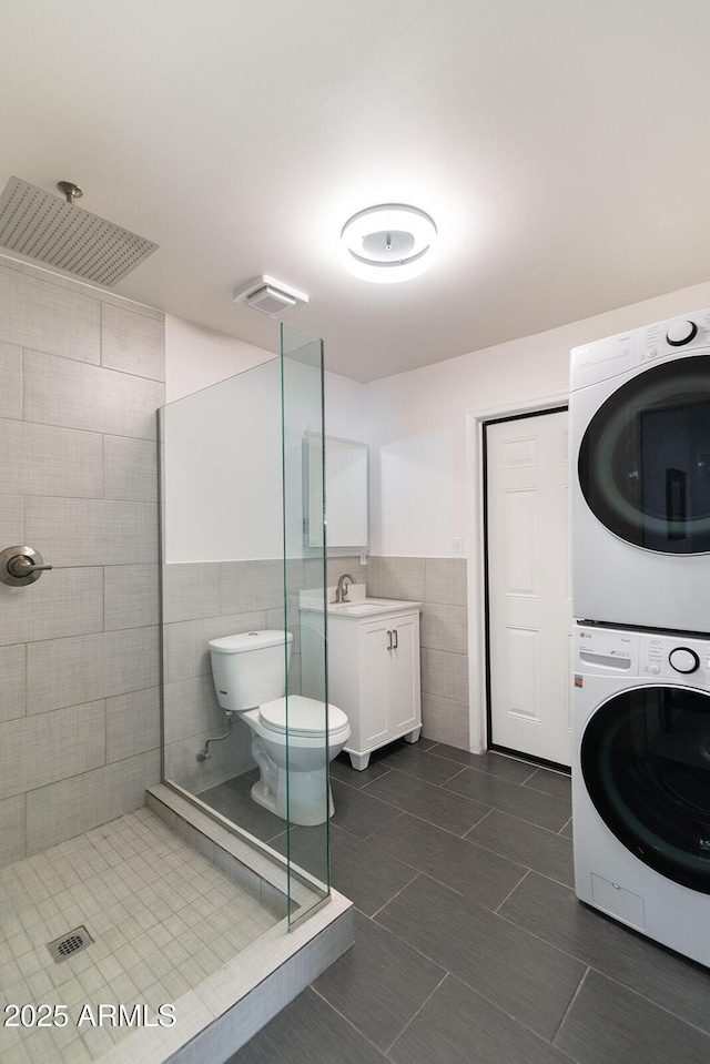 bathroom featuring vanity, tile patterned floors, toilet, stacked washing maching and dryer, and tile walls