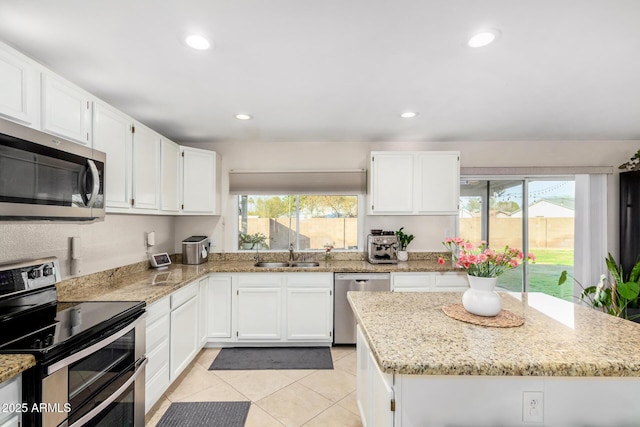 kitchen with sink, light tile patterned floors, appliances with stainless steel finishes, white cabinetry, and light stone countertops