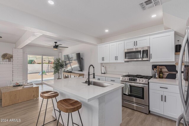 kitchen with an island with sink, stainless steel appliances, sink, and white cabinetry