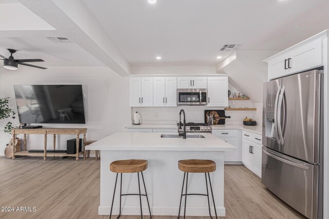 kitchen featuring light wood-type flooring, a kitchen island with sink, white cabinets, stainless steel appliances, and ceiling fan