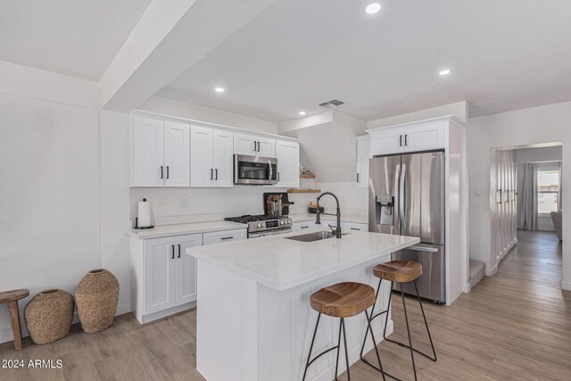 kitchen with light wood-type flooring, sink, an island with sink, white cabinets, and appliances with stainless steel finishes