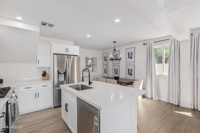 kitchen with white cabinets, sink, a center island with sink, stainless steel appliances, and light wood-type flooring