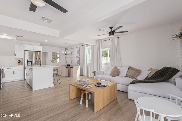 living room featuring ceiling fan with notable chandelier, light hardwood / wood-style floors, beam ceiling, and sink