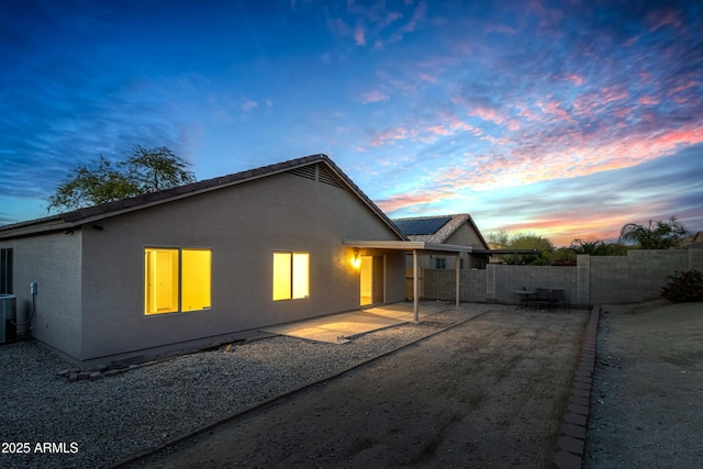 2021 E Caldwell St, Phoenix, AZ 85042 - back of property at dusk featuring a fenced backyard, stucco siding, solar panels, central AC unit, and a patio area