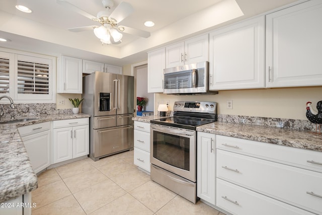 kitchen with stainless steel appliances, a tray ceiling, ceiling fan, sink, and white cabinetry